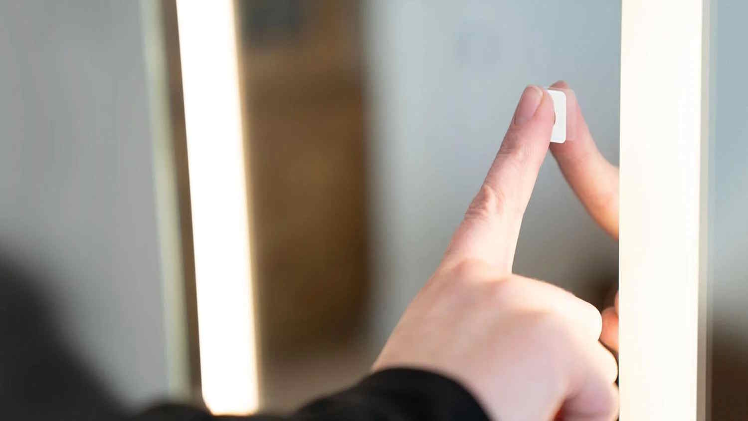 Woman's hand touching the Seura Touch Control Upgrade in a mirror